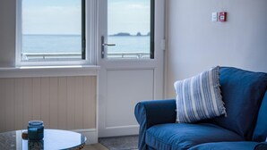 Una habitación con vistas al mar a través de amplios ventanales, un sofá azul con un cojín a rayas y una pequeña mesa redonda con una vela.