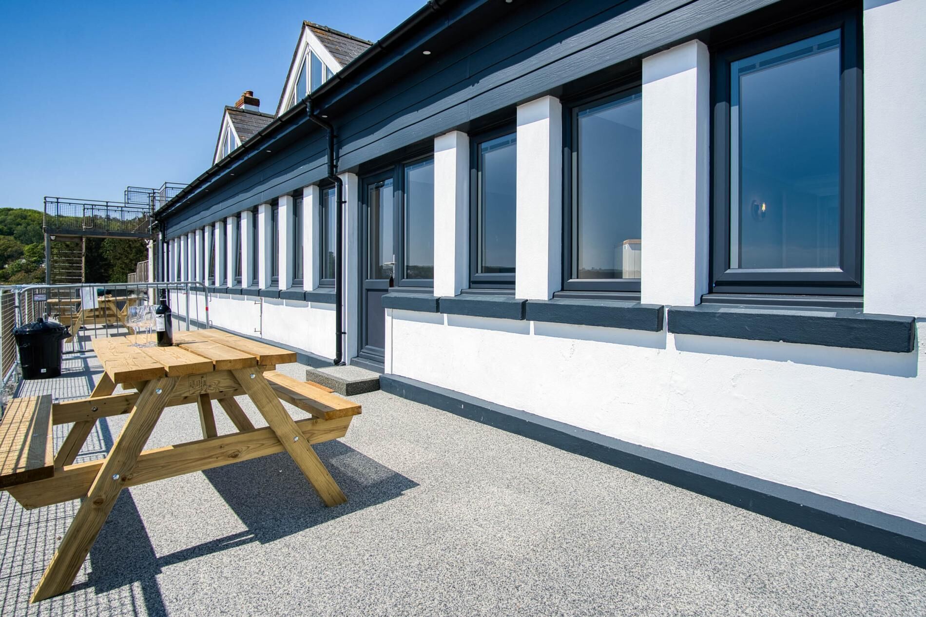 A building with large windows, a wooden picnic table, and a clear sky.