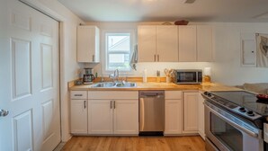 A modern kitchen with white cabinetry, a stainless steel dishwasher, a microwave, and an oven.