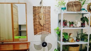 A room with a wooden desk, a green chair, a white fan, a mirror, a wall-mounted shelf with potted plants, and a woven wall hanging. - Amwani Residence - Kalikasan Homes (Puerto Princesa)