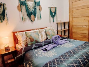 A neatly made bed with patterned bedding, a wooden headboard, and decorative wall hangings.