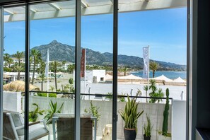A balcony with a view of a beach, palm trees, and mountains. - 3095 Elegant Beachside Apartment in Puerto Banús (Marbella)