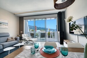 A modern living room with a sofa, coffee table, and dining table set with blue glassware and a white rose.