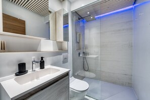 A modern bathroom with a white sink, black soap dispenser, and a glass shower enclosure.