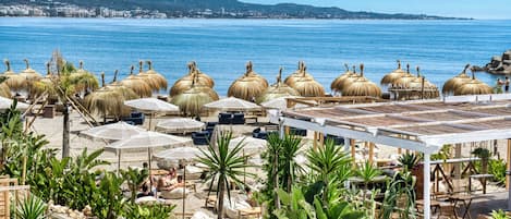 Un resort frente al mar con sombrillas de paja, sillas de descanso y plantas en macetas.