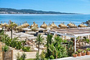 A beachside resort with thatched umbrellas, lounge chairs, and potted plants. - 3095 Elegant Beachside Apartment in Puerto Banús (Marbella)