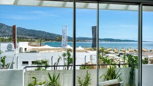 Un balcón con vista a una playa y montañas. Hay banderas y sombrillas en la playa.