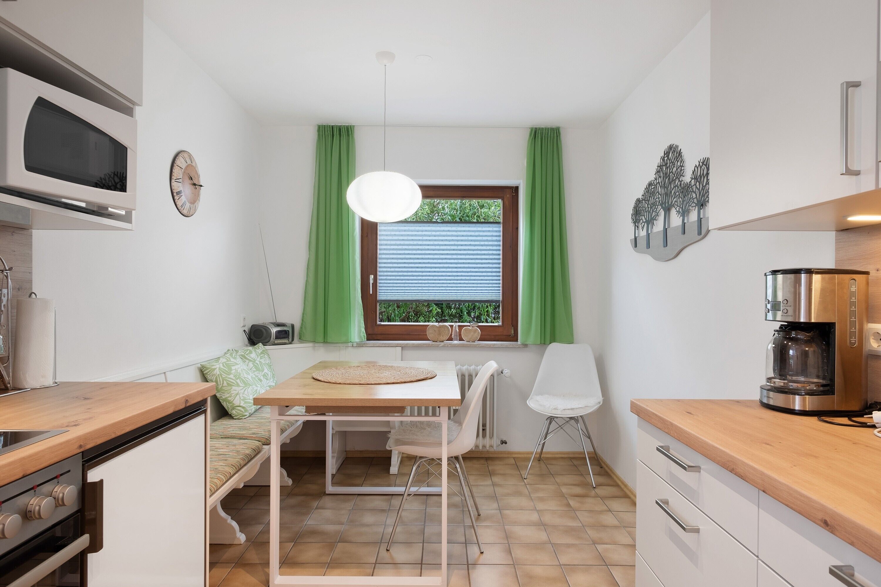 Eine kompakte Küche mit Essbereich, einer eingebauten Mikrowelle, einer Kaffeemaschine und einem Fenster mit grünen Vorhängen.