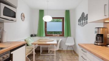 Eine kompakte Küche mit Essbereich, einer eingebauten Mikrowelle, einer Kaffeemaschine und einem Fenster mit grünen Vorhängen.