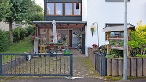A building with a garden entrance, a wooden fence, and signs indicating 'Ferienwohnung' and 'Gästezimmer'.