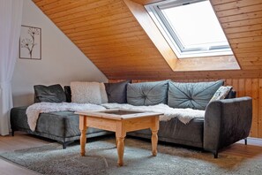 Ein Loft-Zimmer mit schrägem Dach, Holzboden, einer Dachfensterkuppel, einem grauen Sofa, einem Holztisch und einem gerahmten Bild an der Wand.