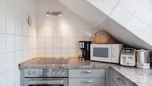 A kitchen with white tiles, a microwave, a toaster, a coffee maker, and a wooden basket on the counter.