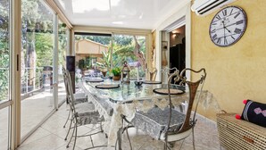 A dining area with a glass table, metal chairs, and a wall clock. - Villa 'Palmiers En Couleurs' with Mountain View, Private Pool, and Wi-Fi (Cuers)