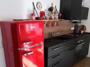 Een compacte keuken met een rode Amica-koelkast, een zwarte spoelbak en een houten aanrecht.