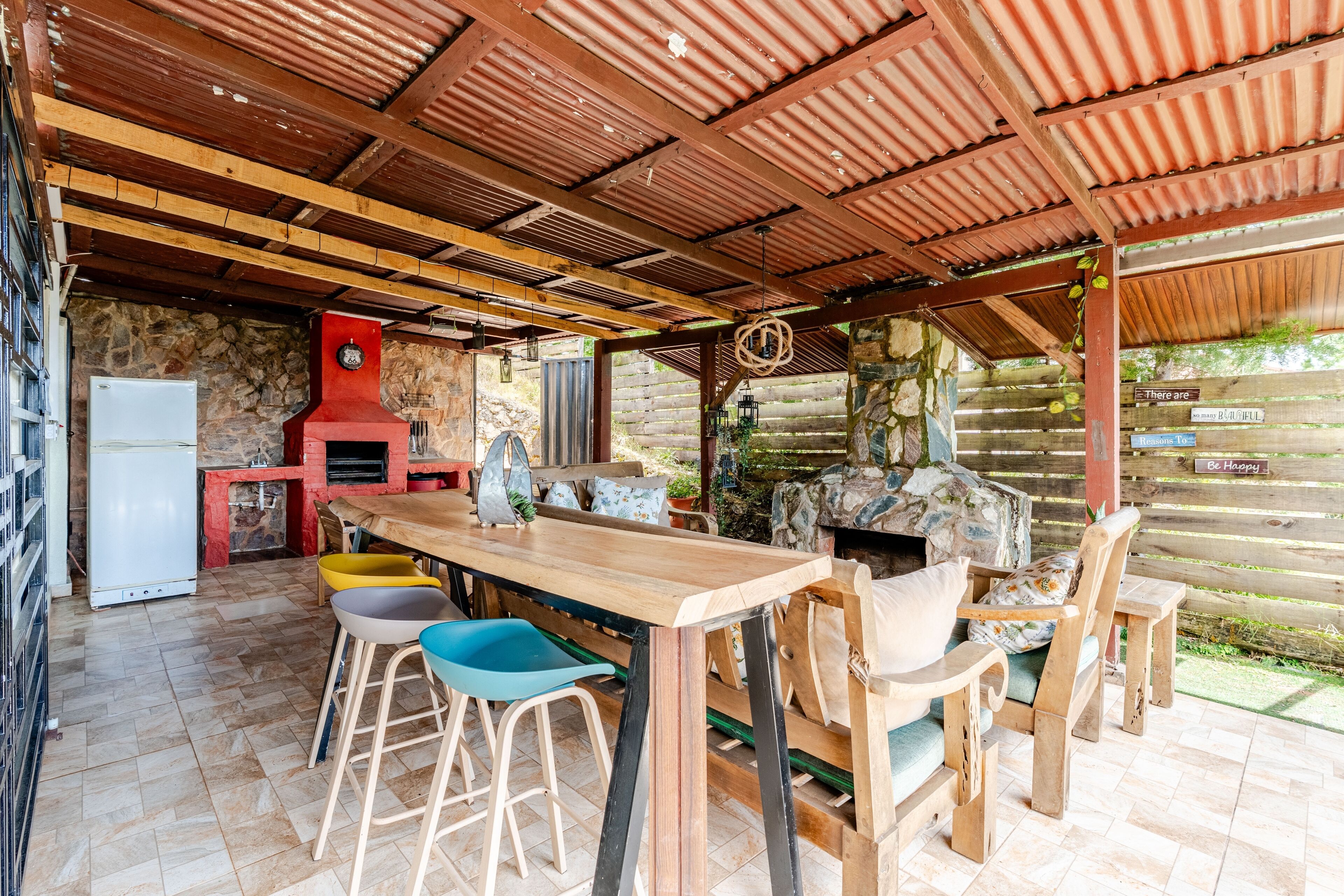 Een rustieke buiten eethoek met een houten tafel en stoelen, een stenen muur en een rode barbecue.