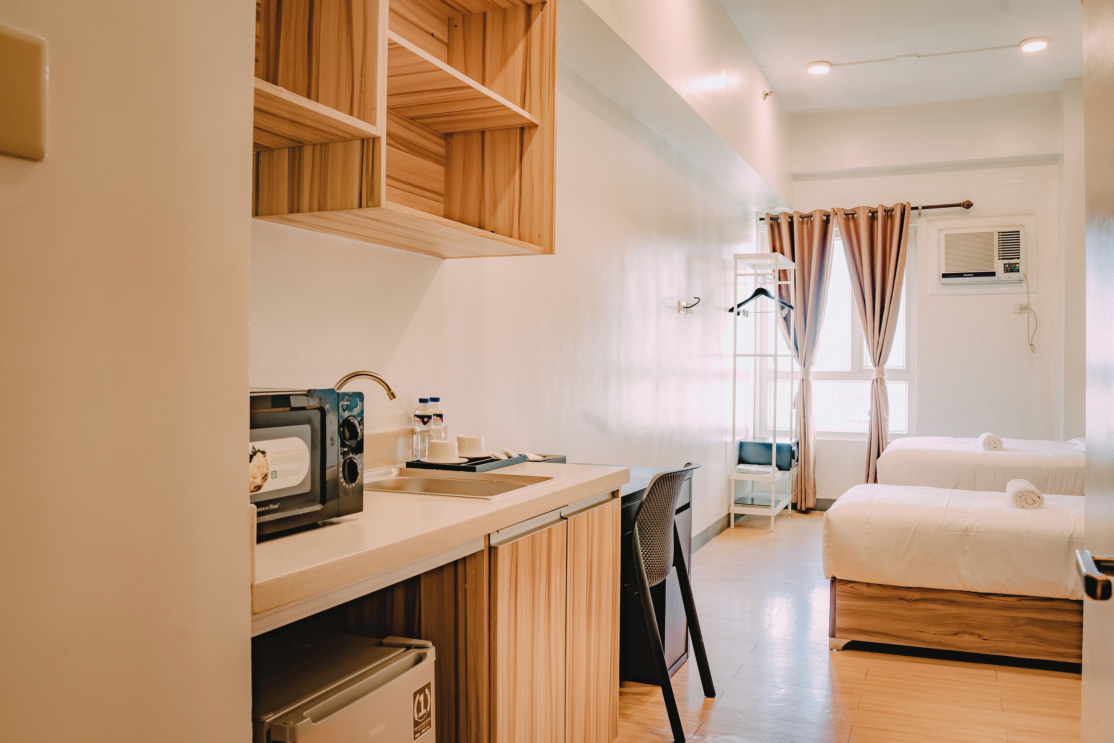 Habitación de hotel con kitchenette, una cama, baño con ducha y ventana con cortinas.