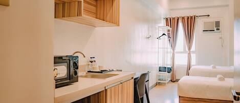 Habitación de hotel con kitchenette, una cama, baño con ducha y ventana con cortinas.