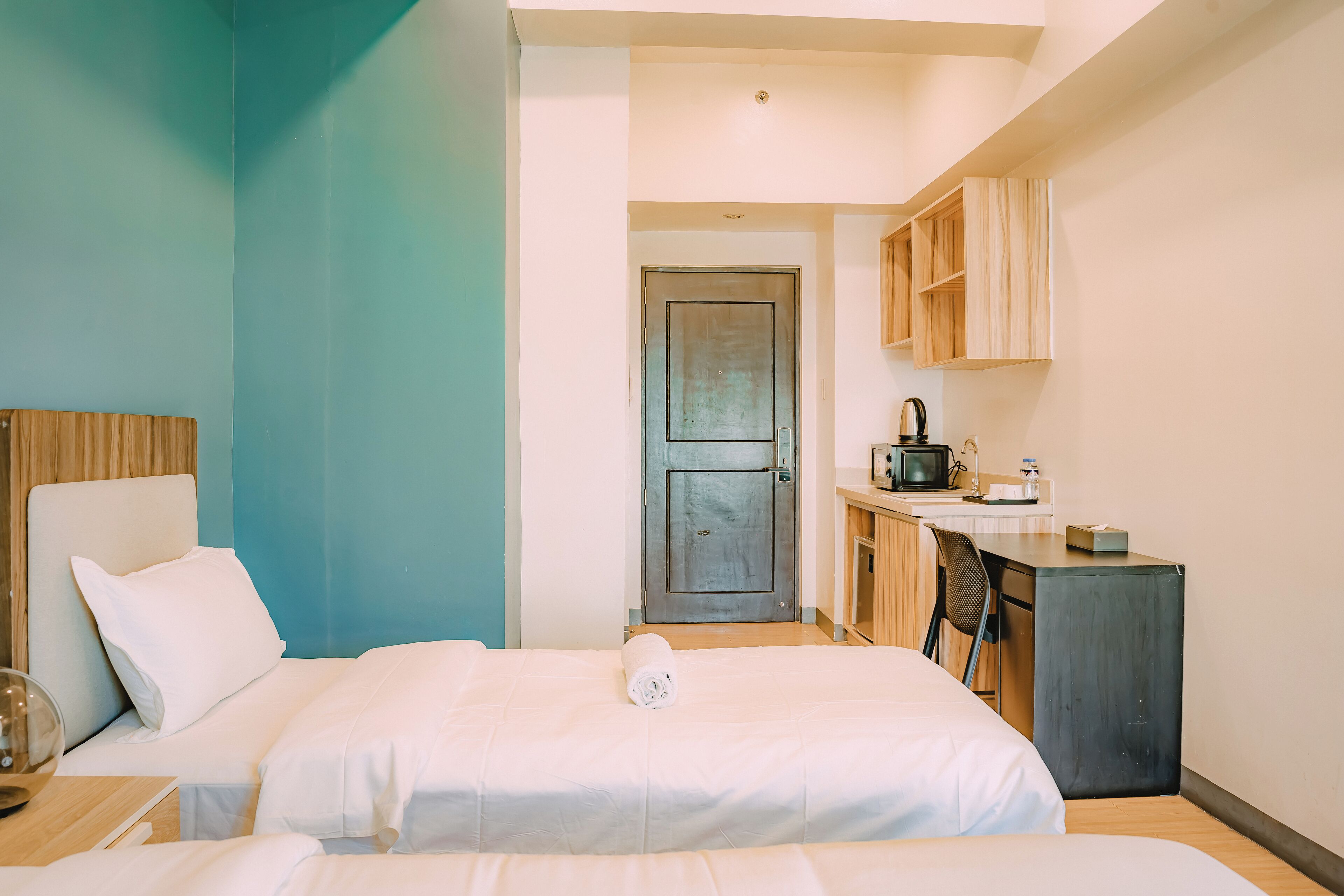 A hotel room with two beds, a desk, a chair, and a kitchenette.