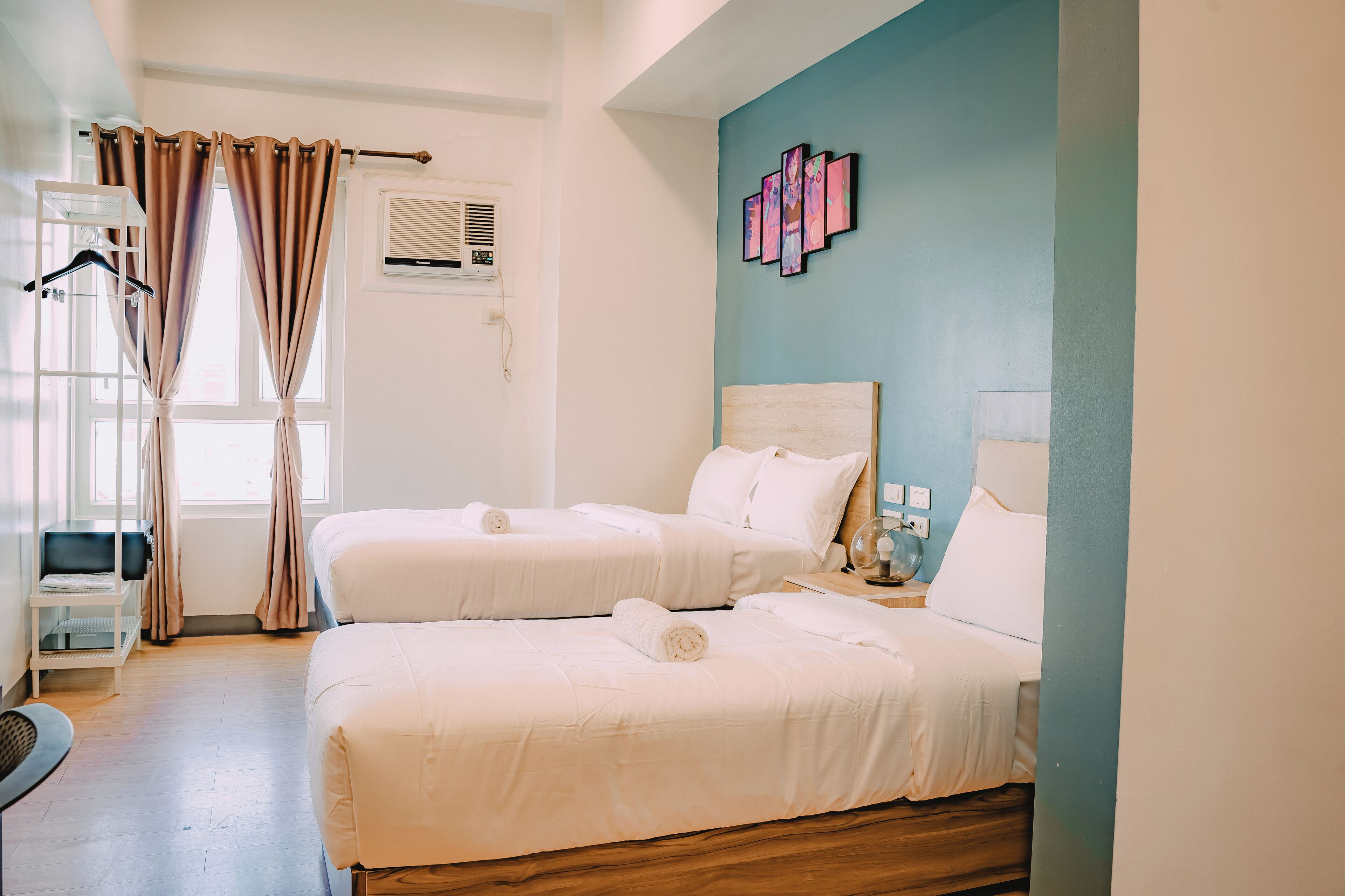 A hotel room with two beds, a desk, a chair, and a window with curtains.