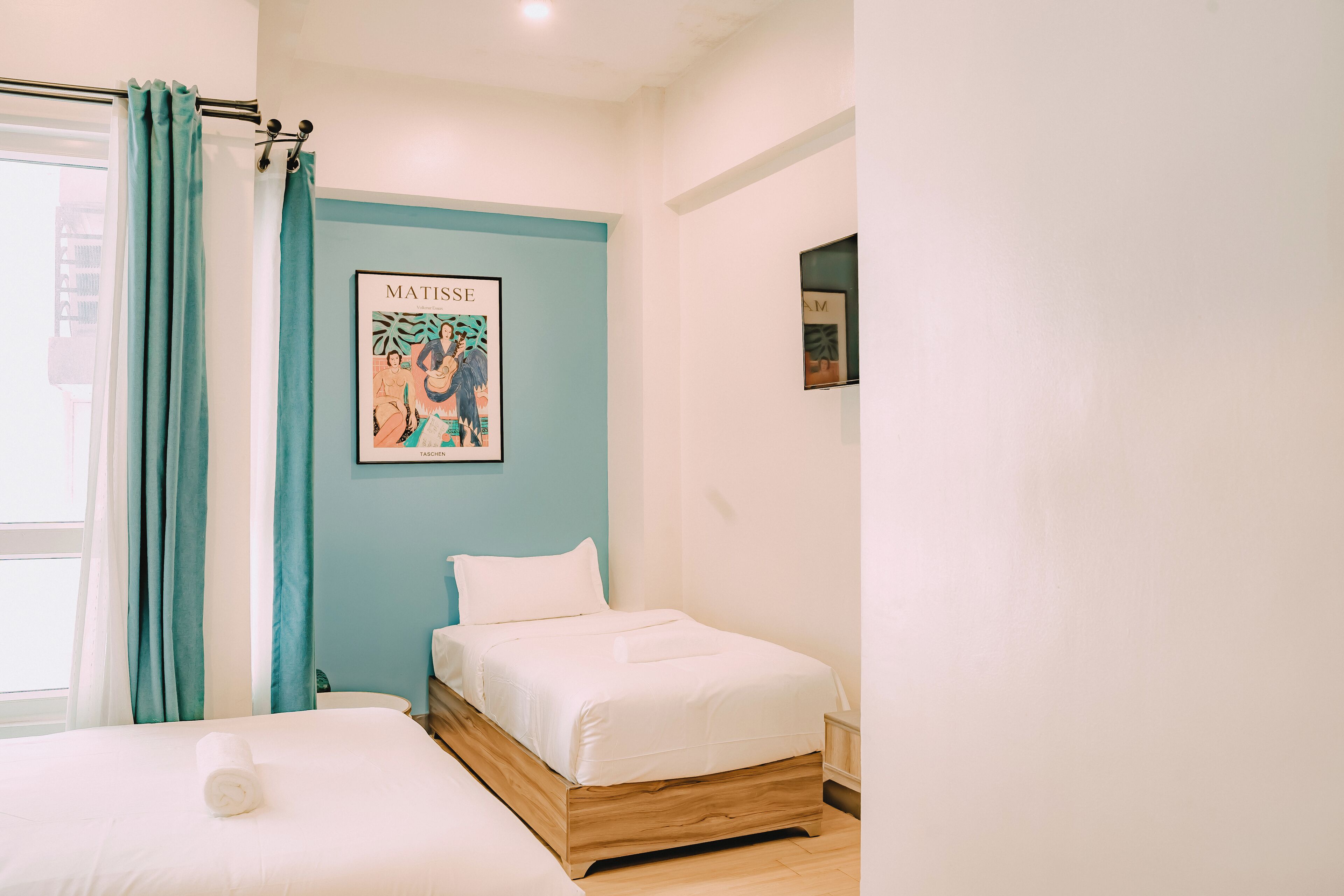 A bedroom with a bed, a window with curtains, and a framed artwork on the wall.