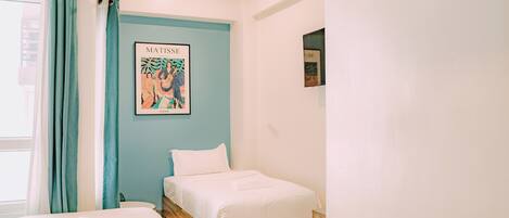 A bedroom with a bed, a window with curtains, and a framed artwork on the wall.