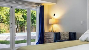 A hotel room with a bed, a nightstand, a lamp, and a view of a swimming pool through glass doors. - Your Hollywood Vacation Home (Hollywood)