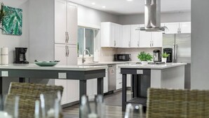 A modern kitchen with white cabinets, stainless steel appliances, and a central island with seating. - Your Hollywood Vacation Home (Hollywood)