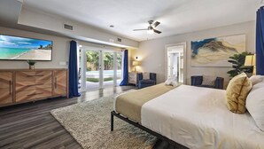 A modern hotel room with a large bed, a TV, a ceiling fan, and a view of a pool through the sliding glass doors. - Your Hollywood Vacation Home (Hollywood)