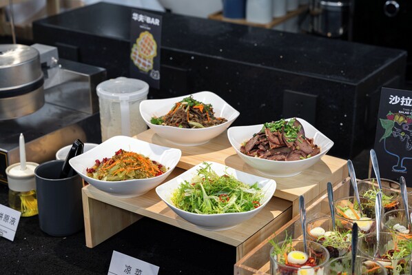 Une table de buffet proposant divers plats, notamment des salades, de la viande et des légumes.