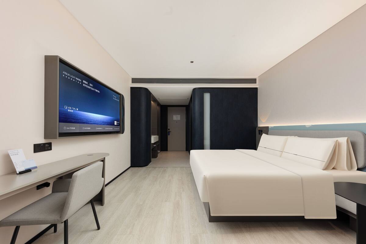 A modern hotel room with a bed, a desk, and a television displaying a menu.