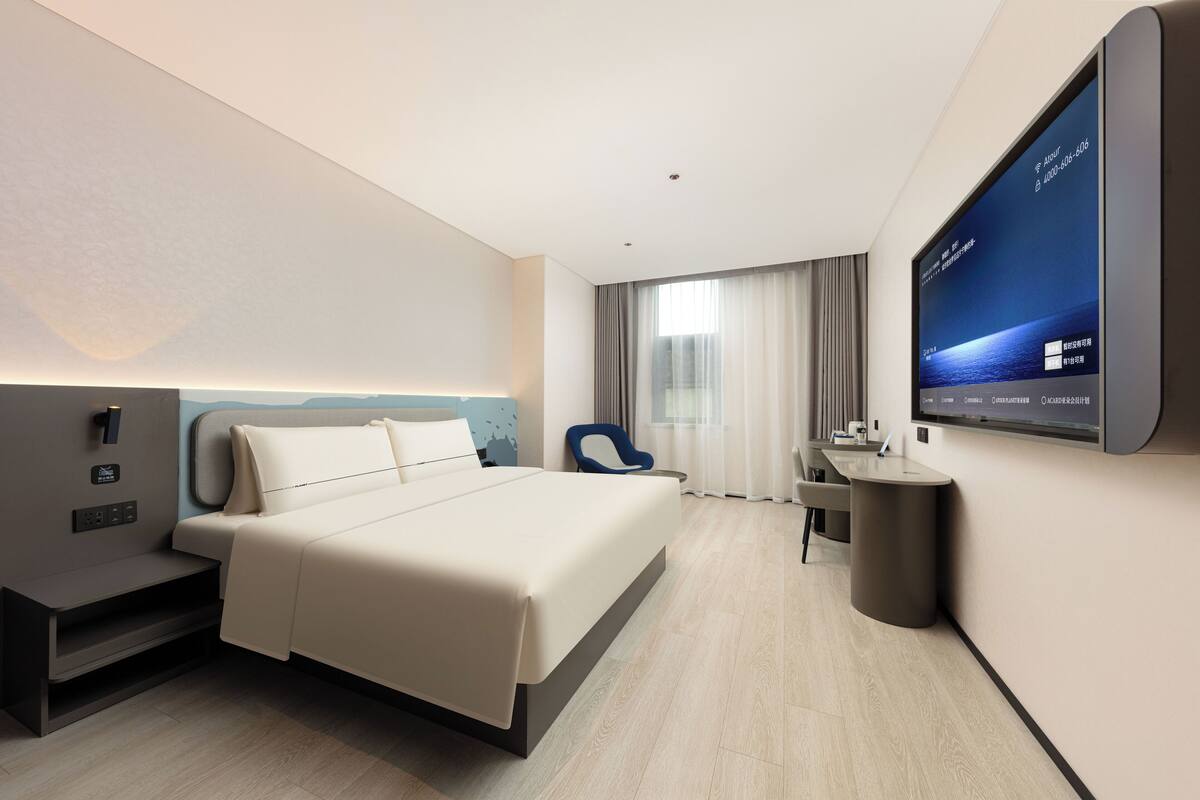A modern hotel room with a large bed, a desk, a chair, and a TV mounted on the wall.
