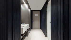 A modern, narrow hallway with a white sink and mirror on the left, a door at the end, and dark paneling on the walls.