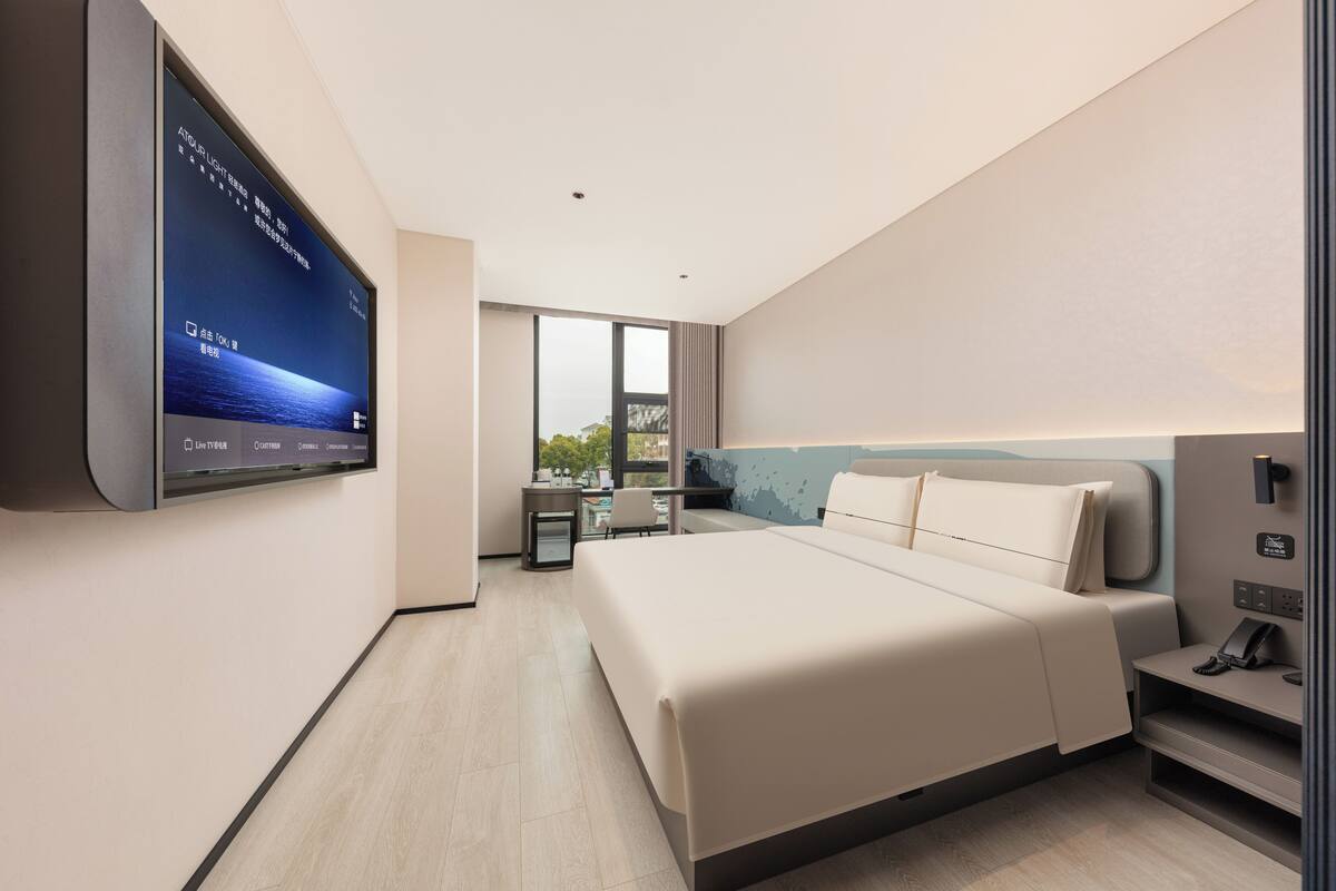 A modern hotel room with a large bed, a desk, and a TV mounted on the wall.