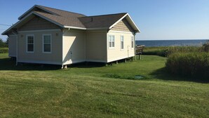 A single-story house with a gabled roof, a front porch, and a view of the ocean.
