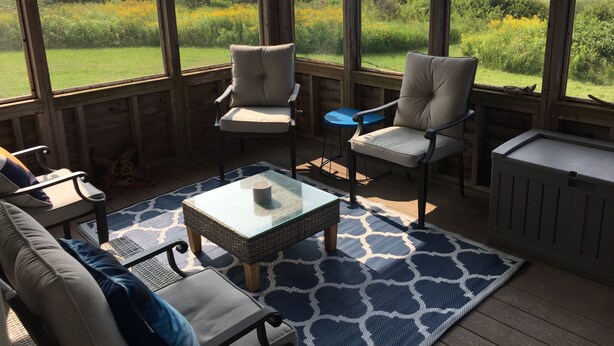 A sunroom with a view of the sea, furnished with two chairs, a table, and a sofa.