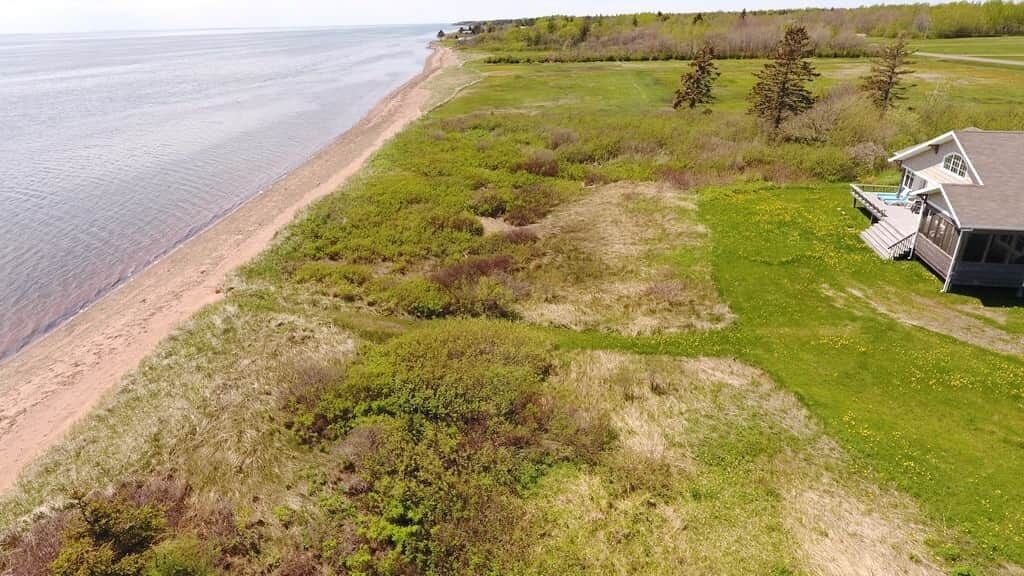 A coastal property with a beach view, a grassy area, and a house with a deck.