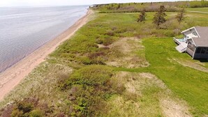 A coastal property with a beach view, a grassy area, and a house with a deck.