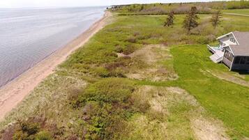 A coastal property with a beach view, a grassy area, and a house with a deck.