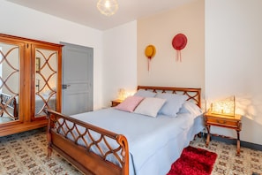 Um quarto com uma cama de madeira, uma mesa de cabeceira com abajur, um espelho e uma porta.