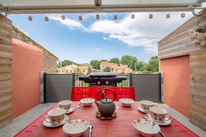 Um pátio externo com uma mesa posta para chá, uma churrasqueira e vista para edifícios ao fundo.