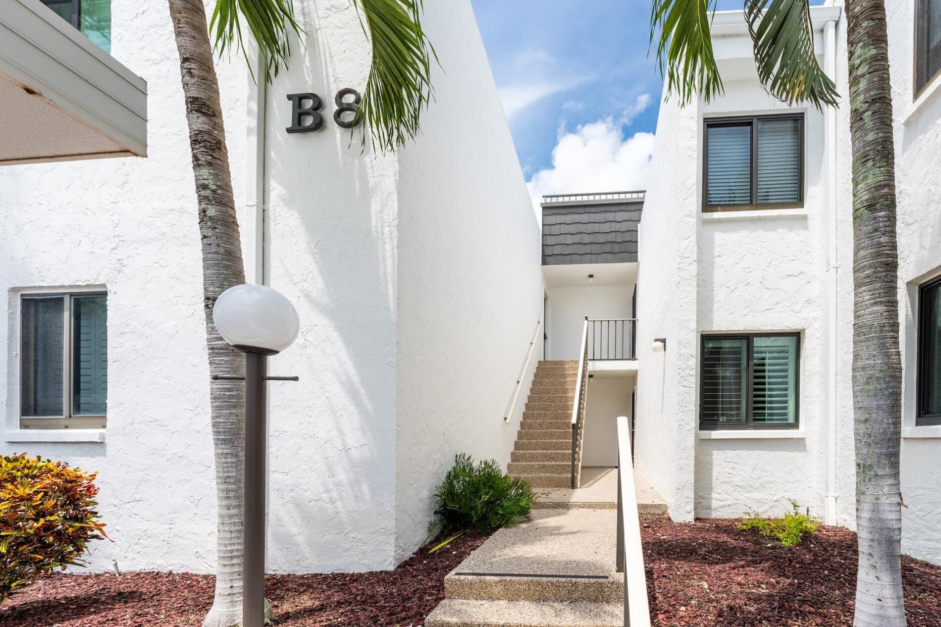 A modern building with a white exterior, a staircase leading to an upper level, and a sign with the letters "B8".