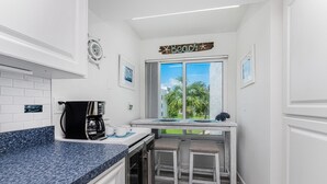 Una cocina con cafetera, una ventana con vista a palmeras y un letrero que dice 'Beach' en la pared.