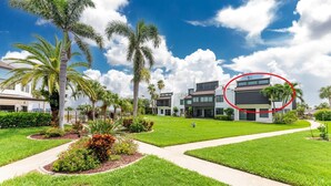 Un área residencial moderna con una casa de dos pisos, rodeada de céspedes cuidados y palmeras.