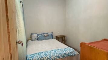 A small, single-bed room with a metal ceiling, a wooden door, and a small table.