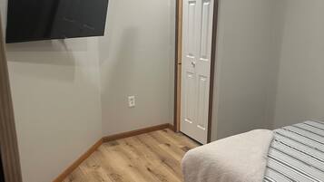 A bedroom with a bed, a flat-screen TV mounted on the wall, and a wooden floor.
