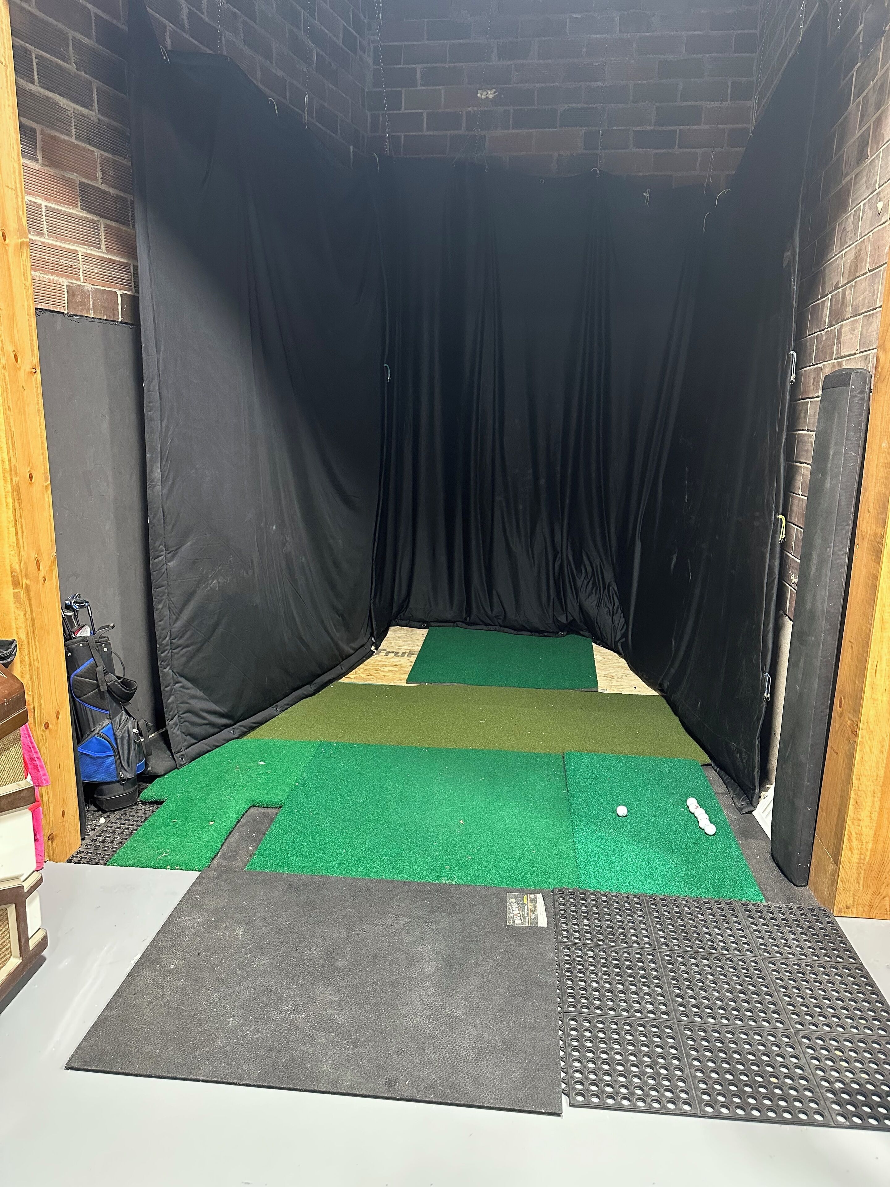A room with a green artificial turf floor, a black mat at the entrance, and a brick wall.