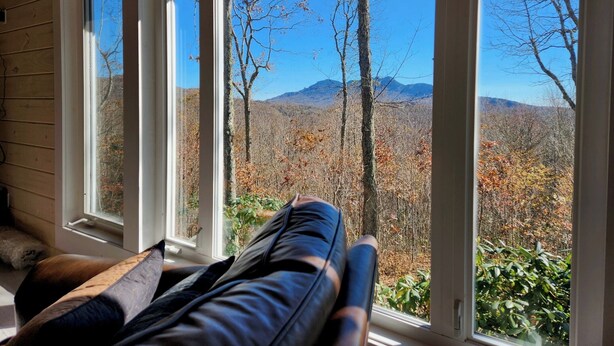 Habitación con un ventanal grande que da a una zona boscosa con montañas al fondo.