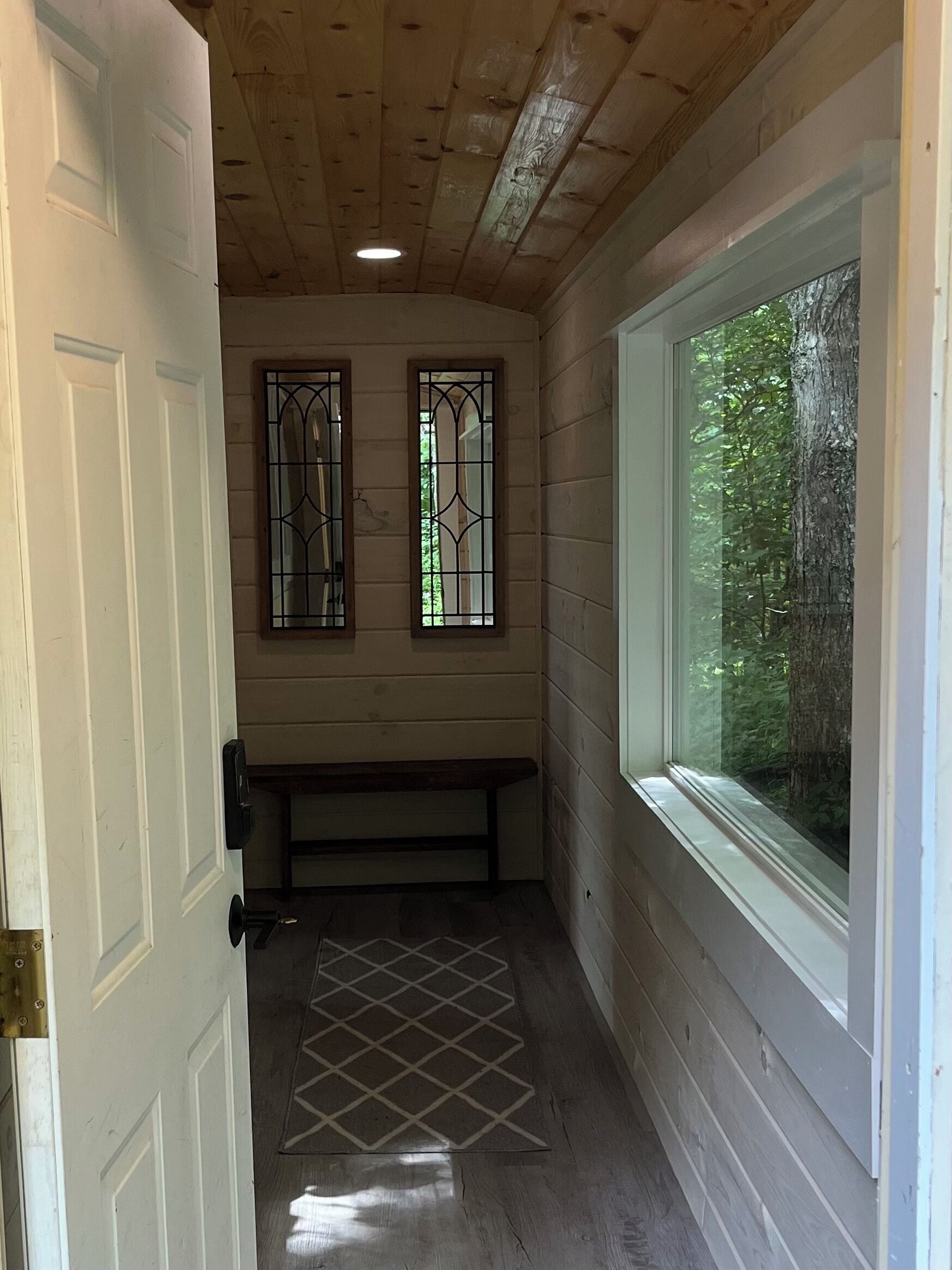A narrow hallway with wooden walls, a bench, and two stained glass windows.