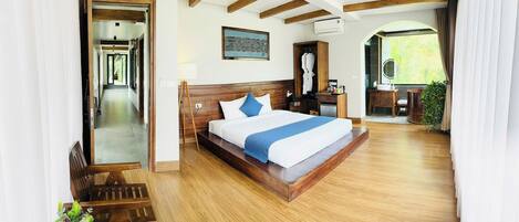 Un dormitorio amplio con una cama grande, vigas de madera, vistas a la vegetación y un baño con lavabo y espejo.