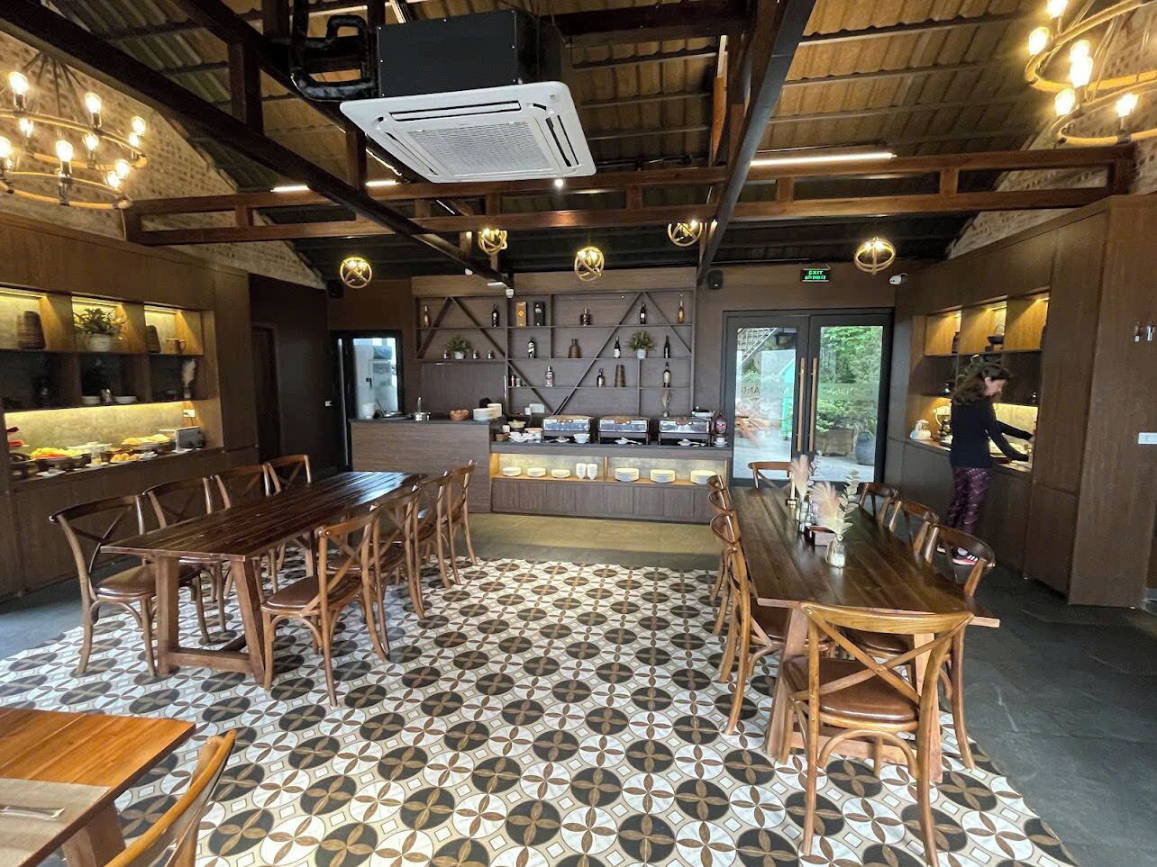 Ein Restaurant mit einer zentralen Bar, Holztischen und -stühlen sowie einem gemusterten Boden.